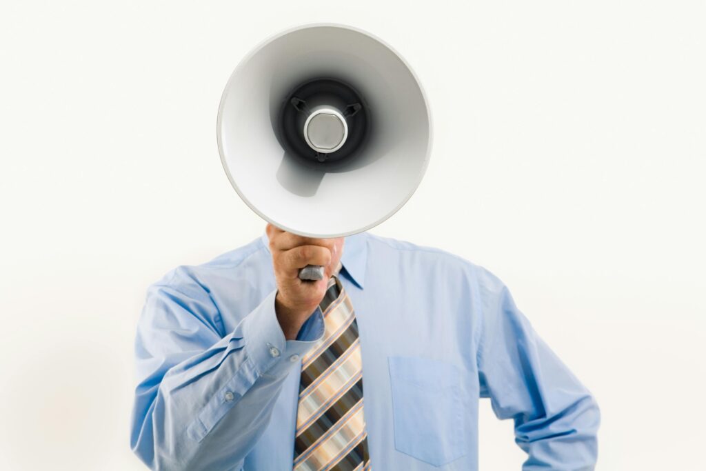 Image pour la page avertissement du blog Serenity Body Mind. Un homme en chemise bleu et cravate en rayure marron et beige, qui tient un mégaphone vers sa tête. #SBM