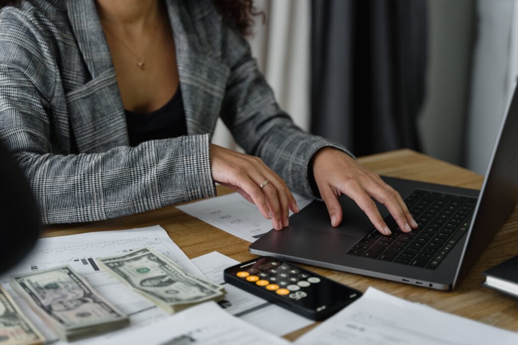 Image article de blog mains d'une femme en train de travailler devant son ordinateur avec à côté une calculatrice et de l'argent en billet sur la table - psychologie finance - Serenity Body Mind