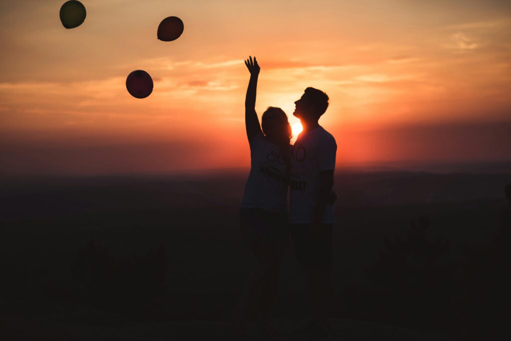 Image pour article de blog sur la st valentin. Image de deux personnes qui avaient lancÃ©s des ballons de fÃªte et en second plan un paysage de couchÃ© de soleil dorÃ©.