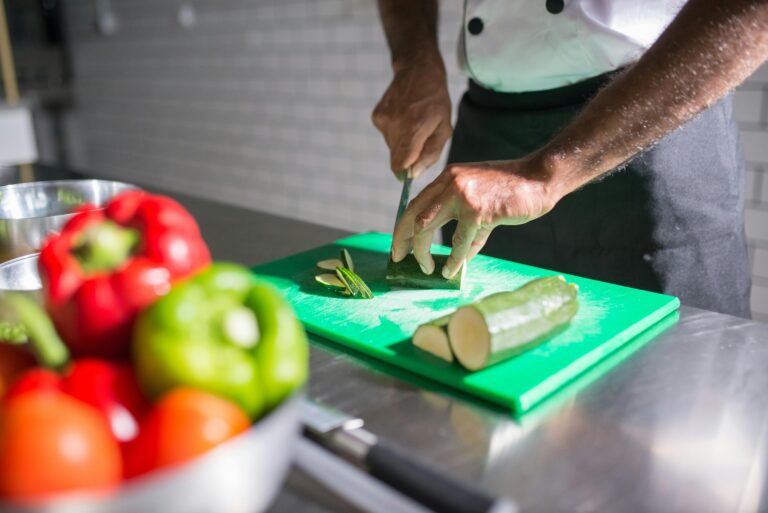 Photo chef cuisiné découpantt courgette sur planche verte, photo contenant aussi poivrons rouge et vert #SBM