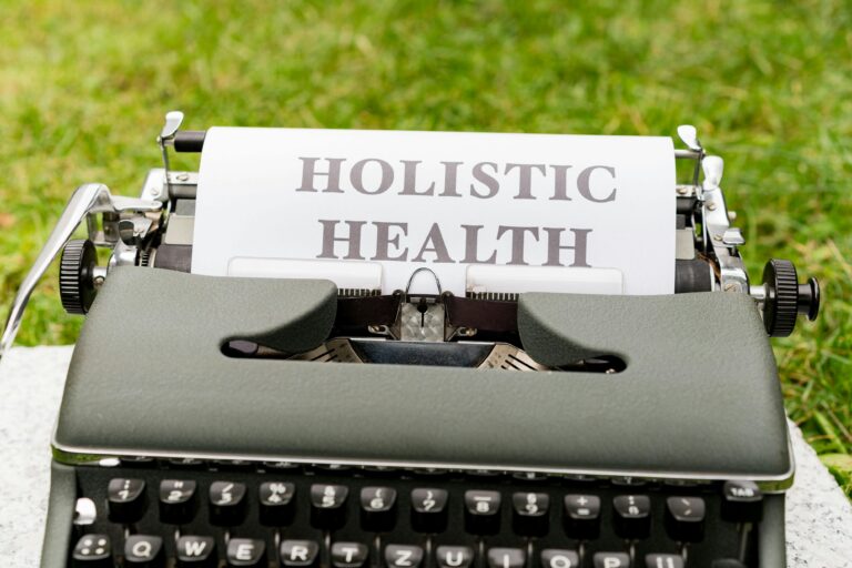 Machine à écrire à l'éxtérieur sur de l'herbe avec feuille écrite "holistic health" en anglais. #SBM #Naturopathie
