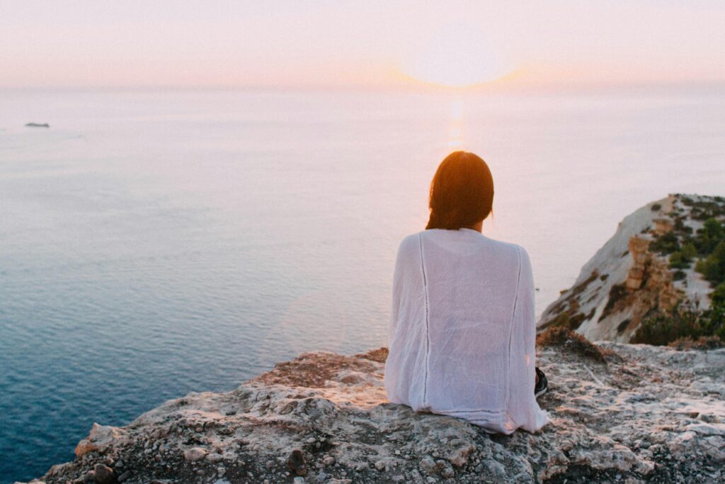 Photo d'une femme assise sur une montagne avec la mer bleu à l'horizon. #SBM #Serenité #mental